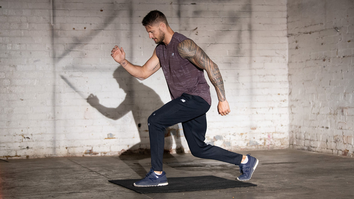A man with tattoos on his arms conducting leg exercises at home performs a lunge.