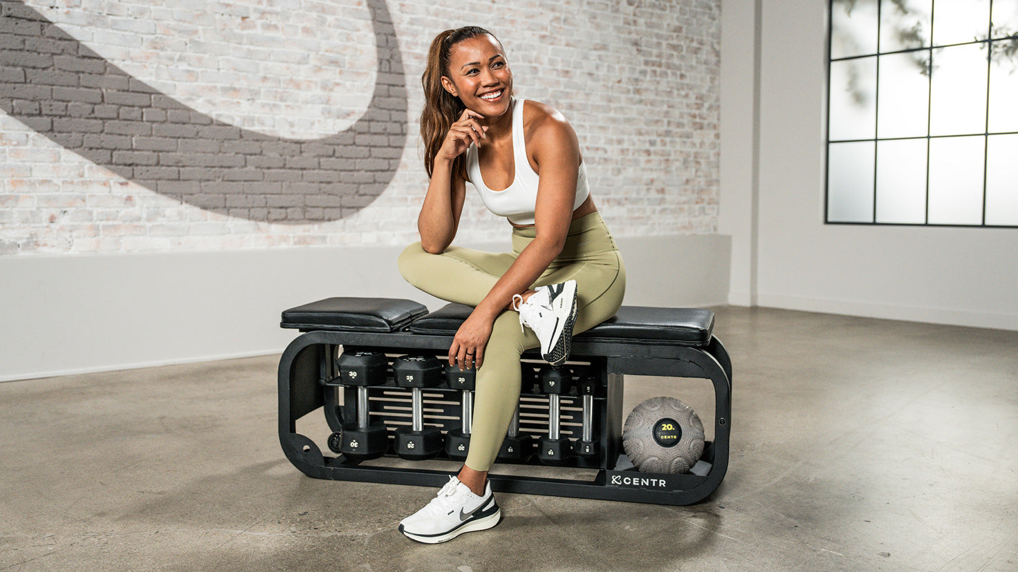 Centr trainer Maricris Lapaix smiles while sitting on a workout bench