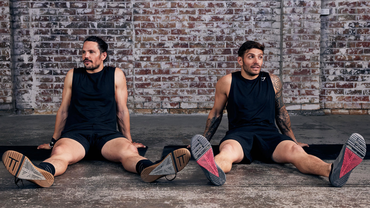 Centr trainers Dan Churchill and Luk Zocchi sit side by side on the gyn floor, legs stretched out in