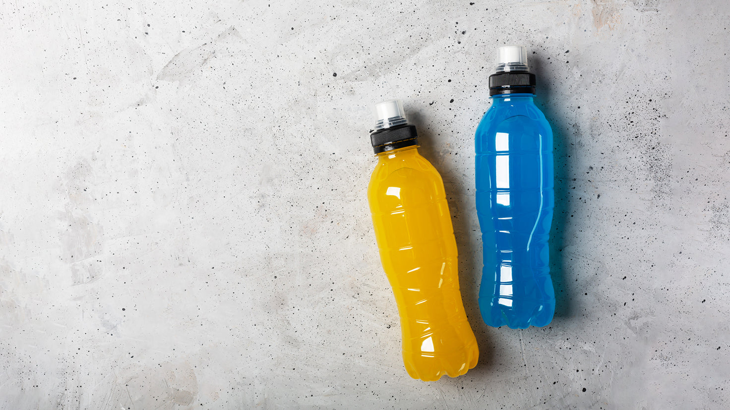 Two bottles of sports drink – one blue and one yellow – lie on the ground.