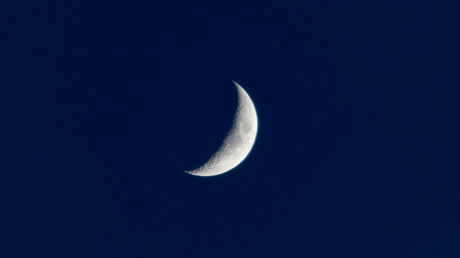 A close-up photograph of a crescent moon against a dark blue night sky.