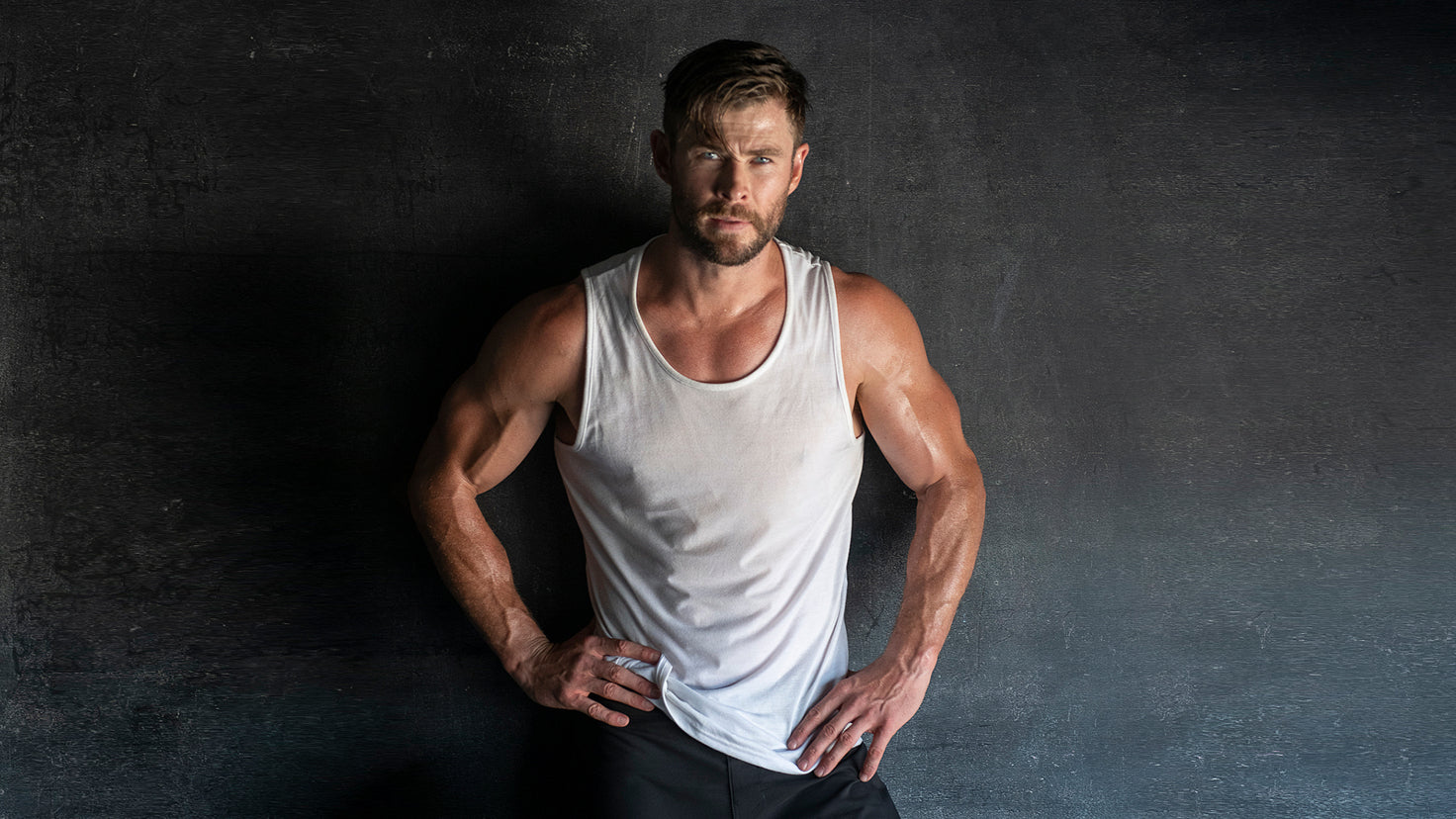 Chris Hemsworth wearing a white tank top, looking intense with muscular arms.