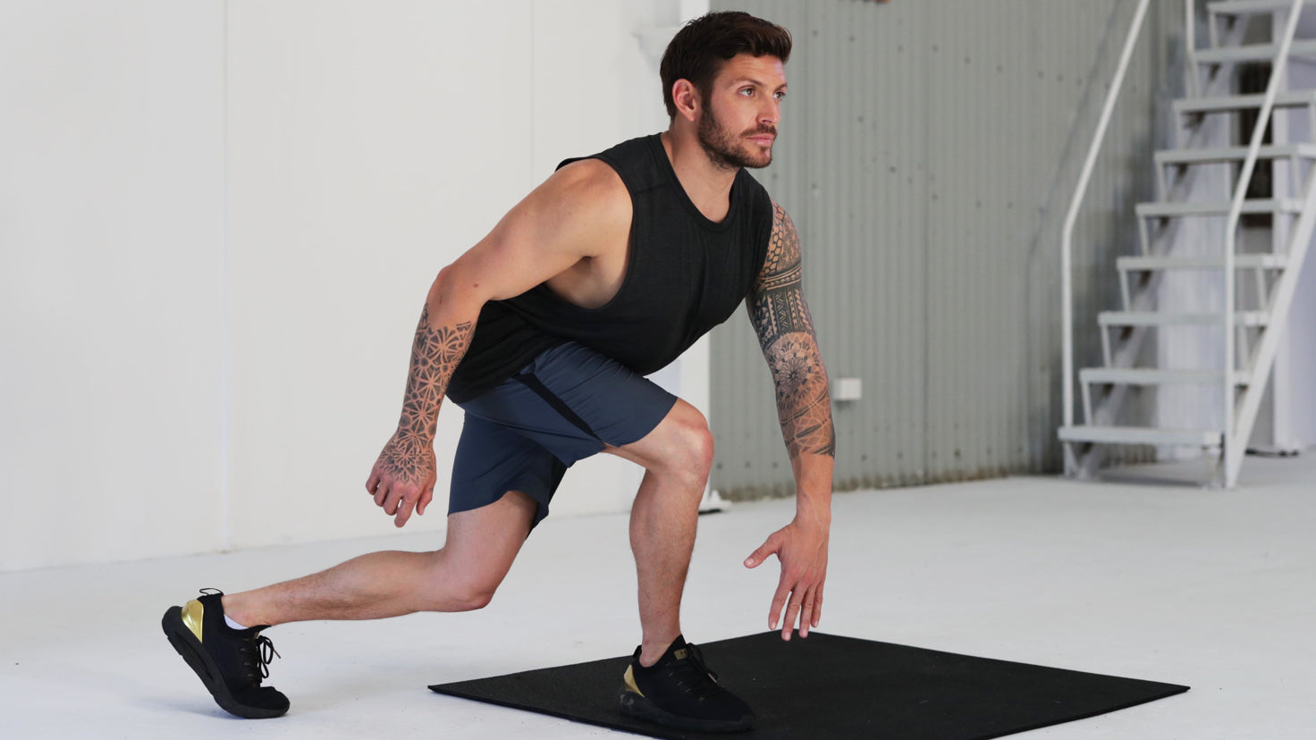 Centr trainer Luke Zocchi, wearing navy gym gear and in a white spacious warehouse gym, performs a c