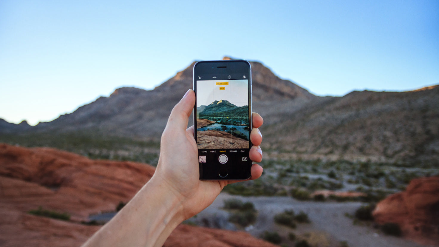 A person holds up a smart phone to take a photo of a mountain landscape.