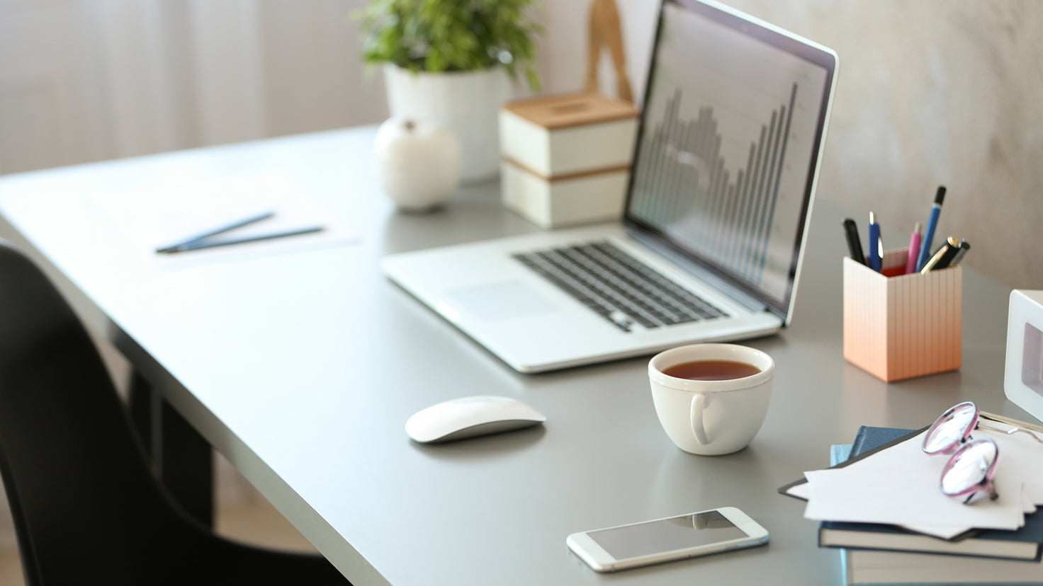 A modern desk with a laptop, cup of tea and organization tools laid out neatly.