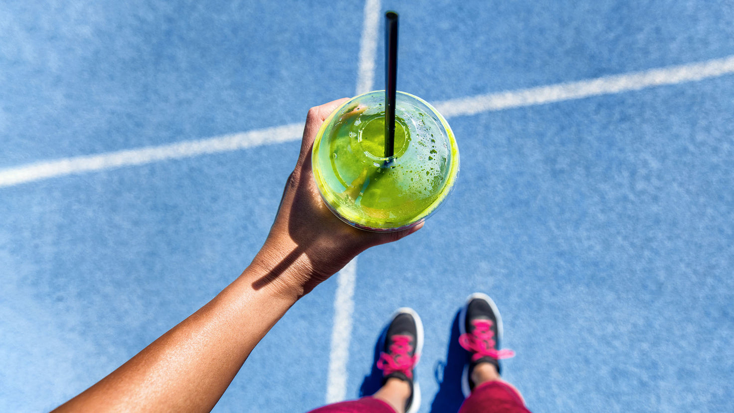 A close-up of a woman holding a green juice in a takeaway cup.