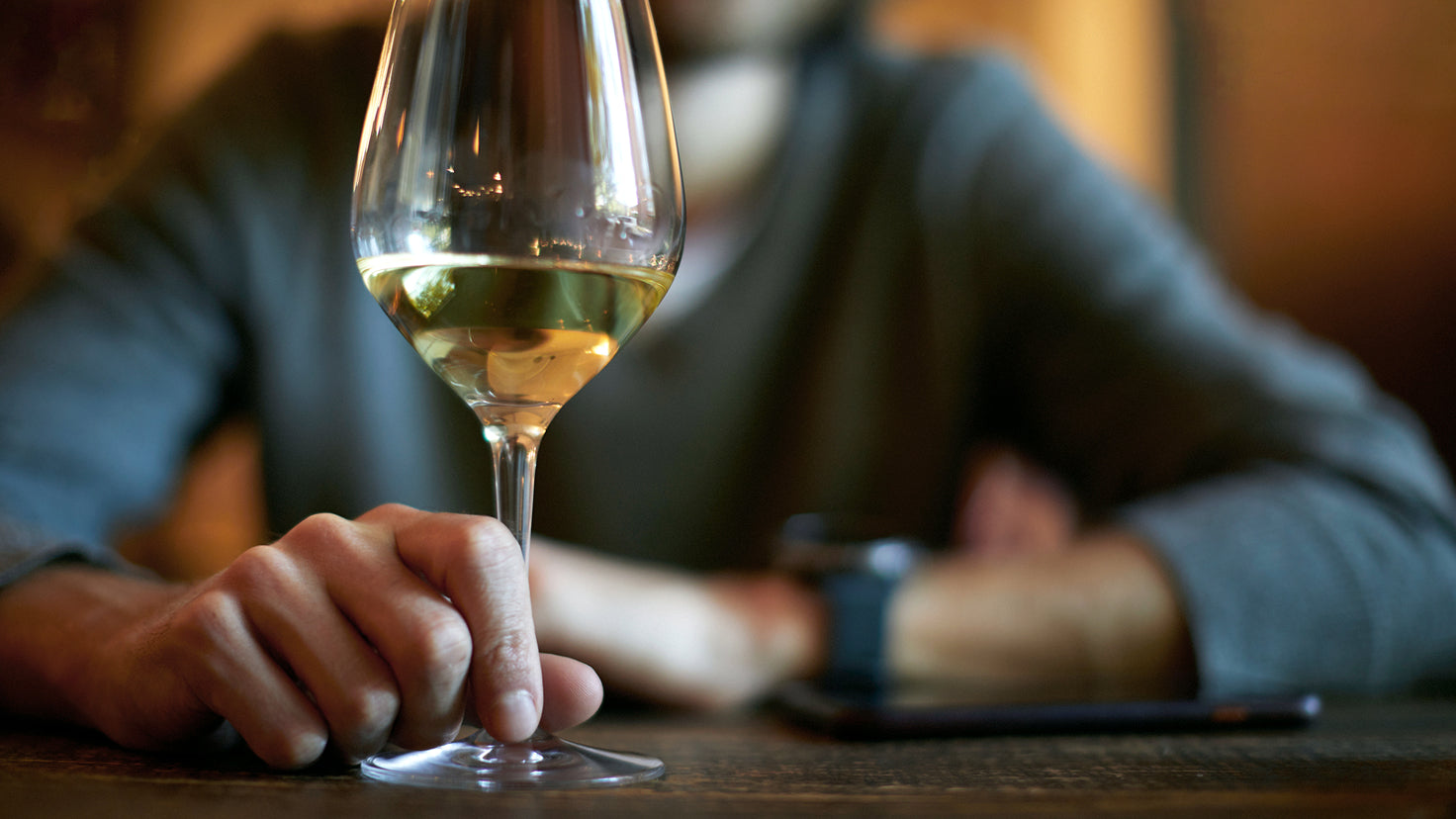 A person drinks a glass of white wine.