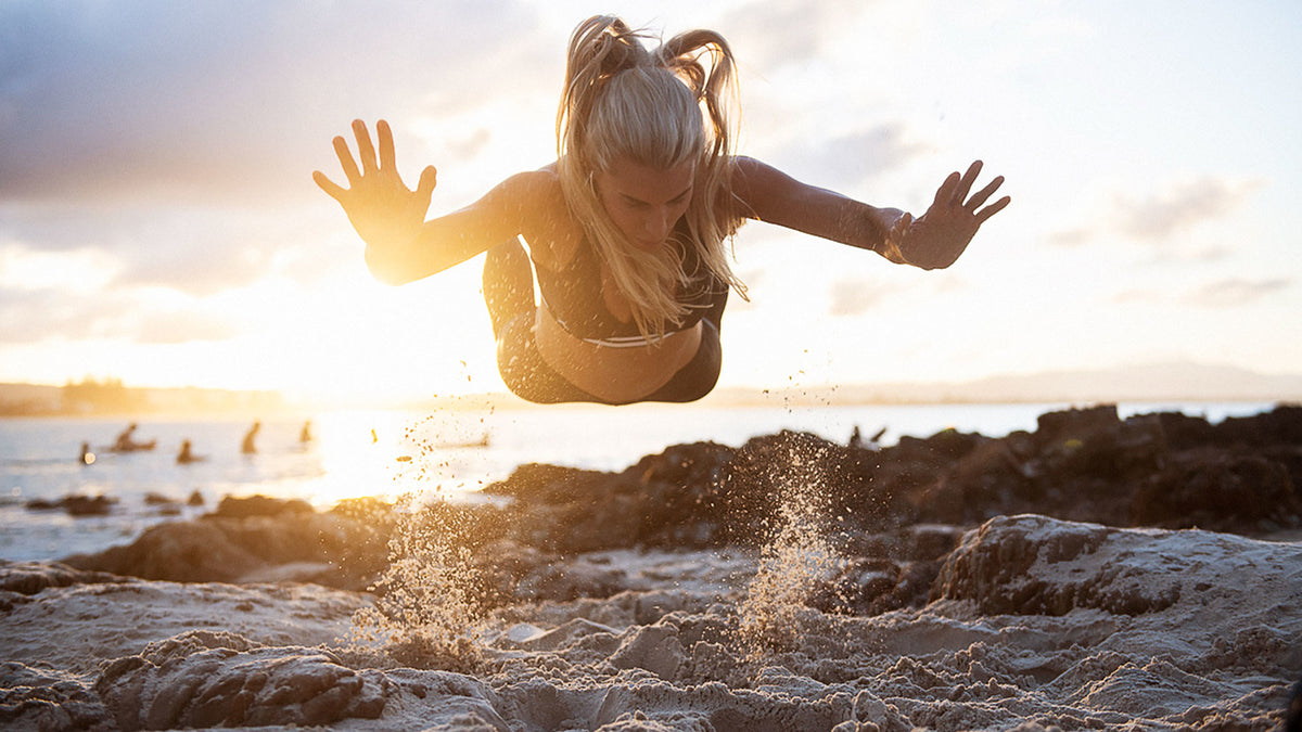 Tiffiny Hall performing a jump push-up on the beach.