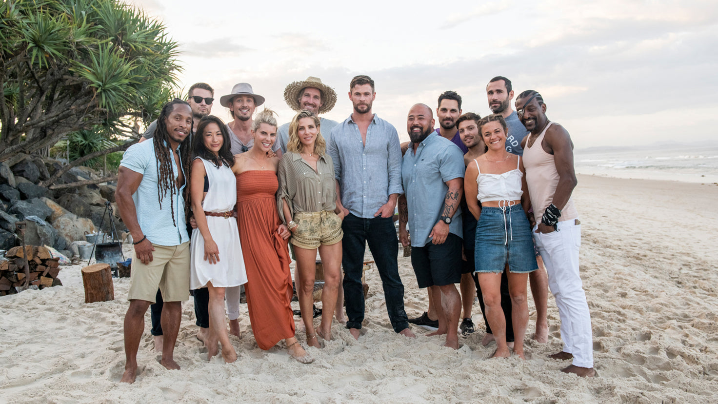 A group of 14 people, including Chris Hemsworth, standing outside on the beach.