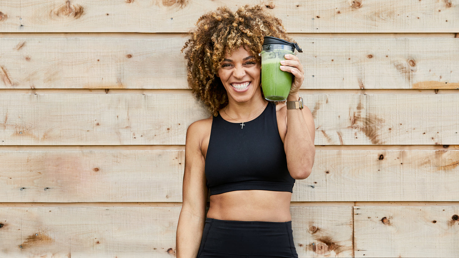 Ashley Joi smiles while holding a green smoothie.