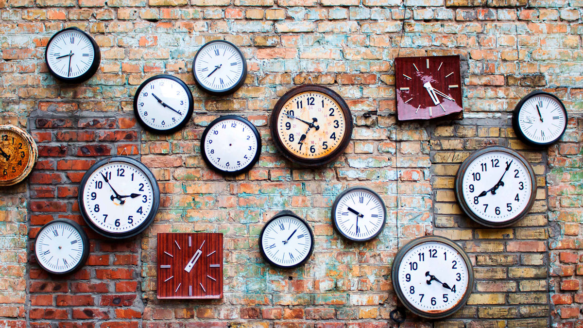 A variety of vintage and new clocks hanging on a red-brick wall.