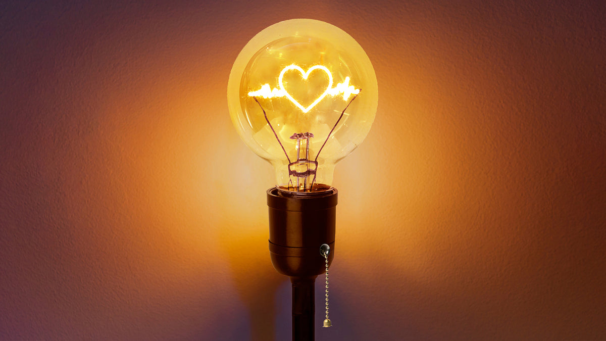 An old-fashioned light bulb with a heart shape formed by electricity.