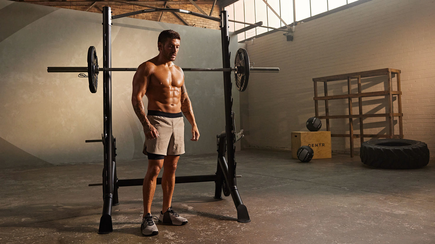 Luke Zocchi stands shirtless in front of a squat rack.