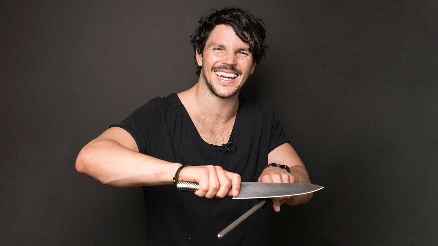 Dan Churchill sharpens a large knife while smiling.