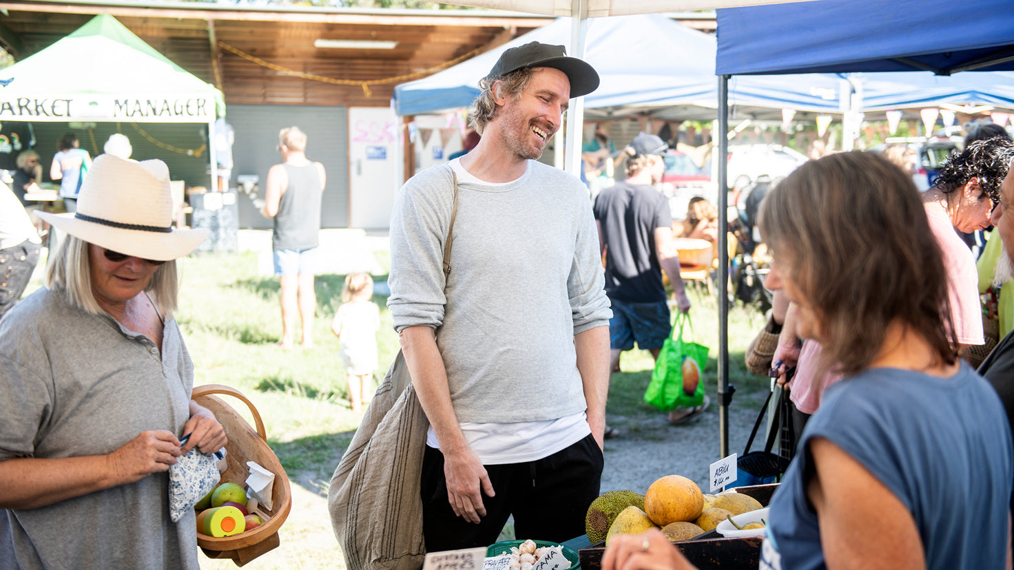 Darren Robertson laughing with a vendor at a Bryon Bay open-air food market.