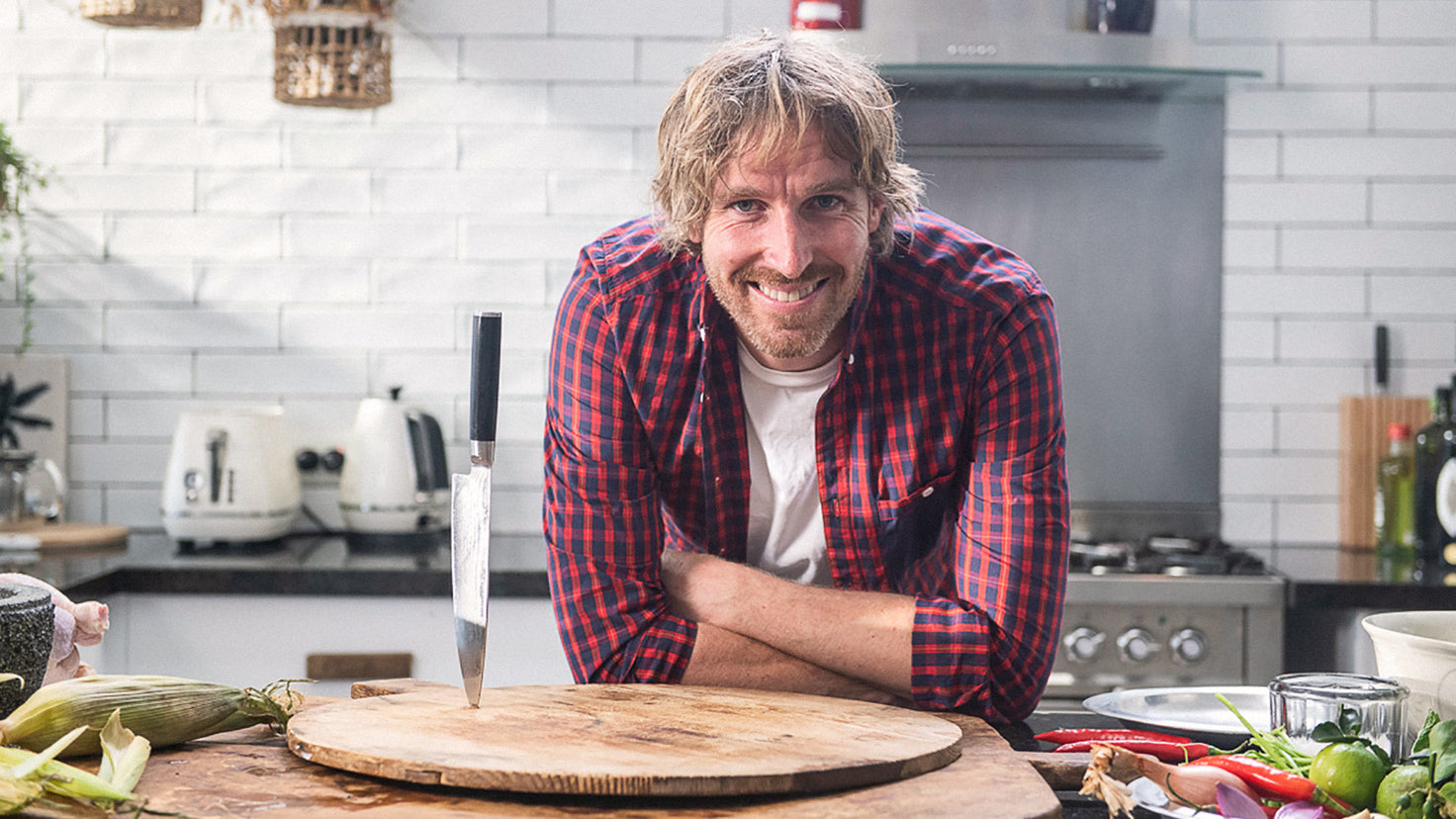 Darren Robertson smiling in a kitchen next to a knife stuck in a chopping board.