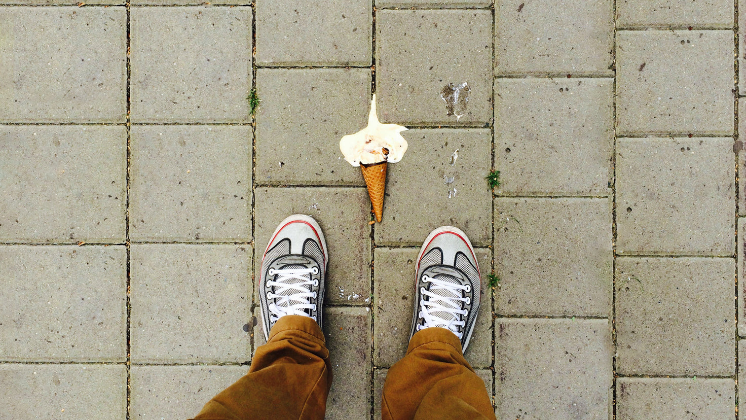 A dropped ice cream cone lies on the ground, melting into the sidewalk.