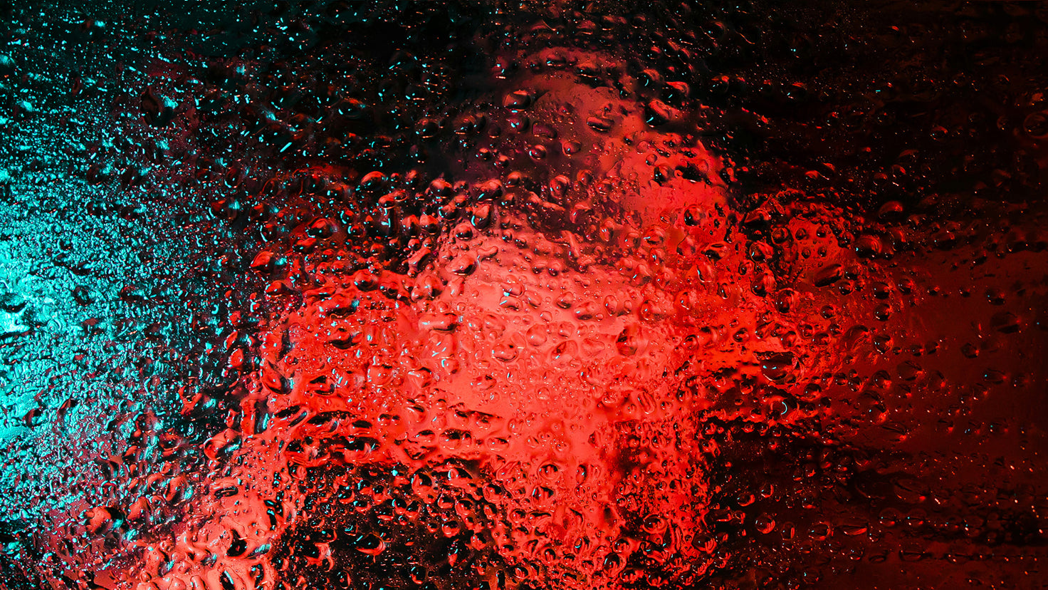 An abstract image of a diffuse red light and dark blue light behind a rippled glass pane covered.