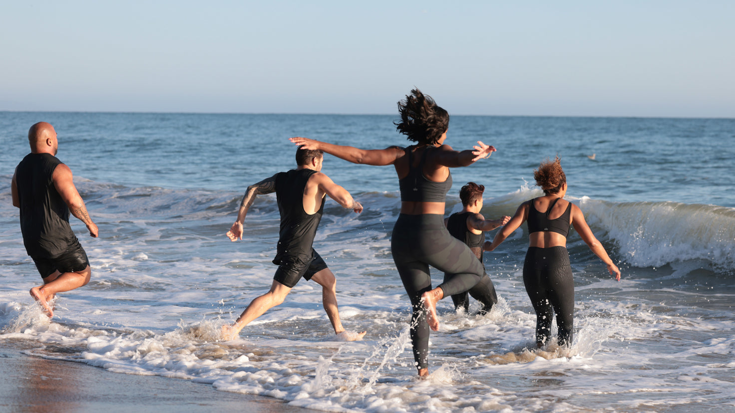 The Centr training team runs joyfully into the surf.