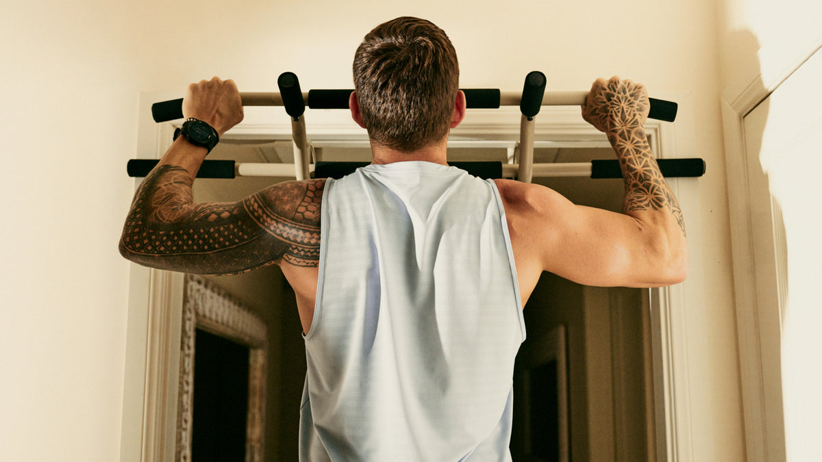 A rear view image of Luke Zocchi performing a  pull-up, using the Centr pull-up bar in a door frame.