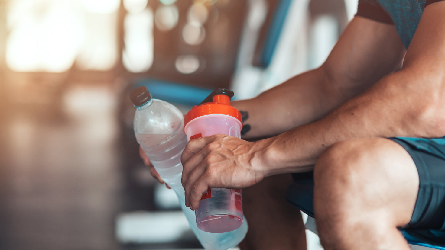 A close-up from the shoulders down of a man holding two water bottles.