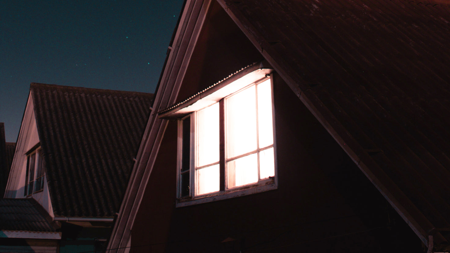 A bright light illuminates a house window on a dark night.
