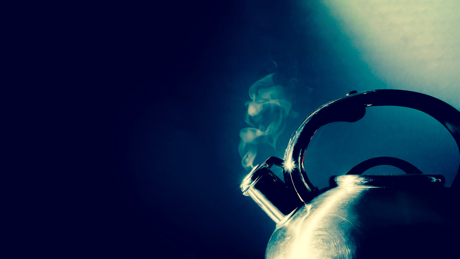 Steam escapes from the spout of a metal kettle.