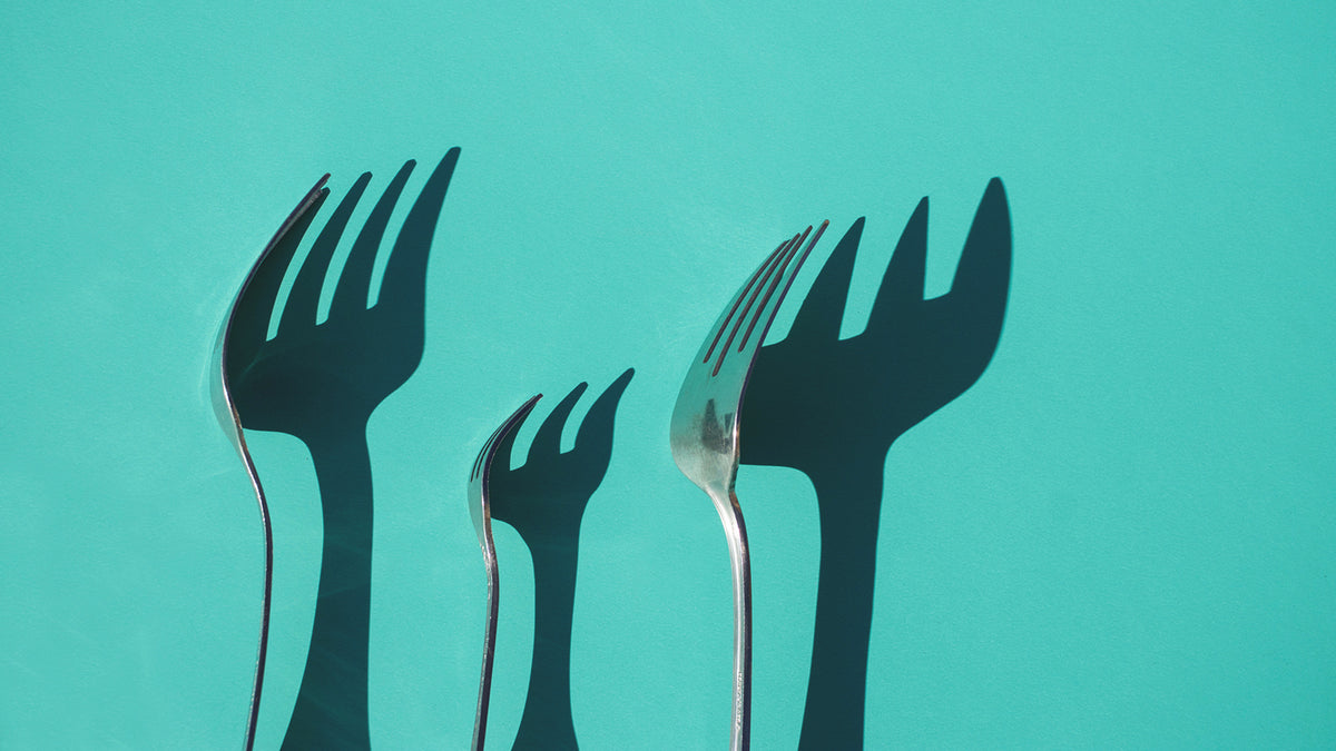 Silver forks casting shadows on a blue wall.