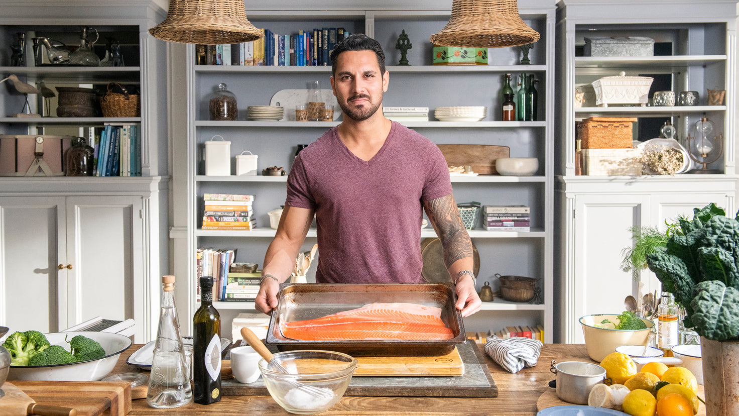 Sergio Perera stands in a kitchen, holding a large pink fish in a baking pan.