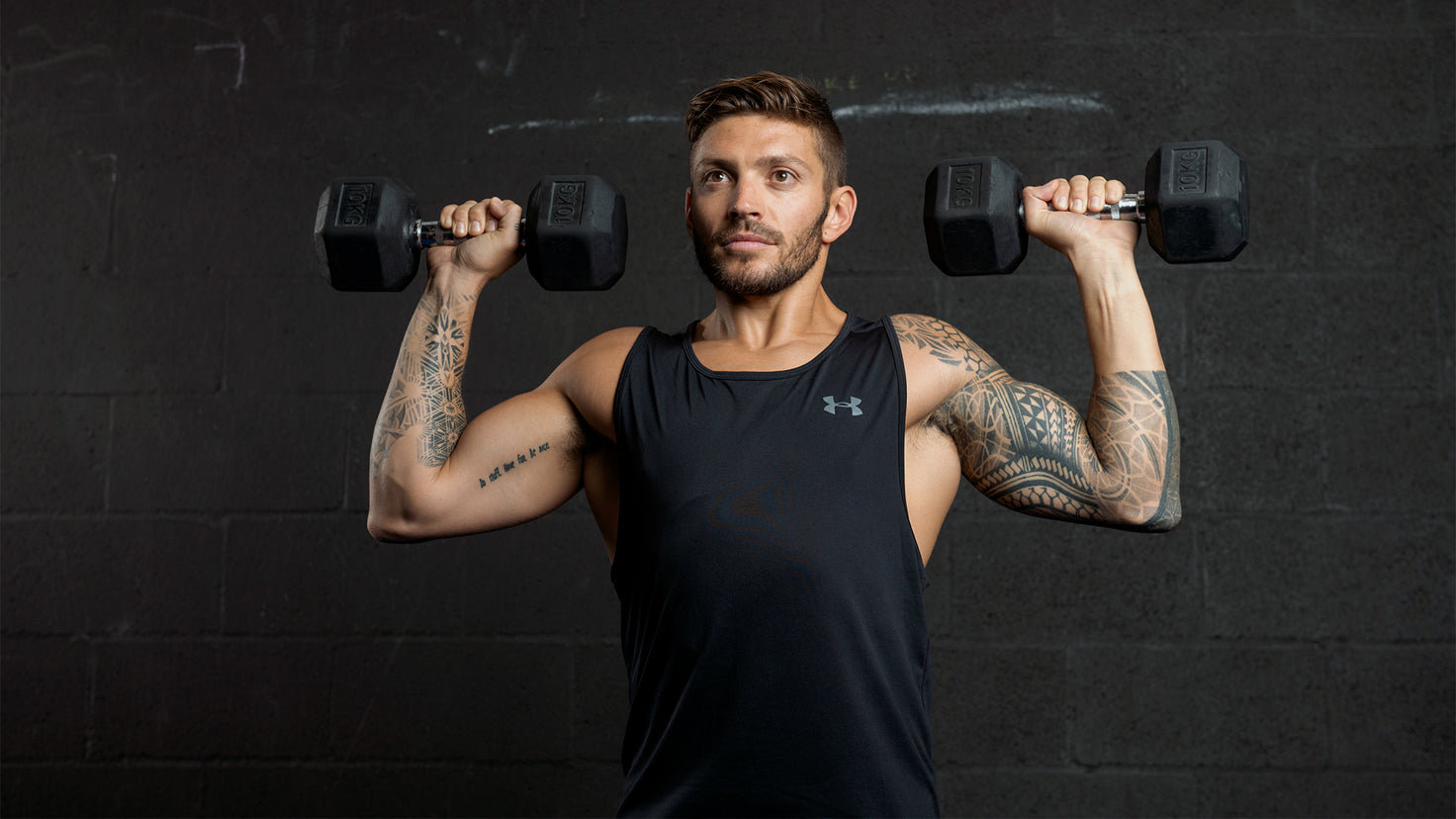 Luke Zocchi performs an overhead press with two heavy dumbbells.