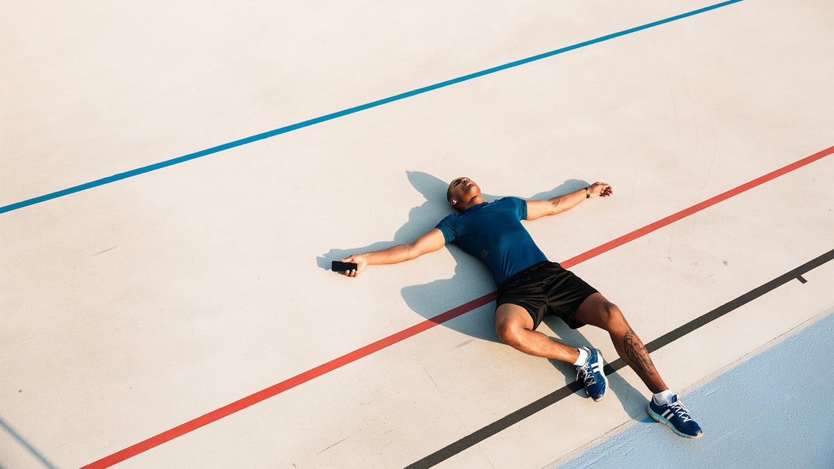 An exhausted man in workout clothes lies on his back on a tennis court.