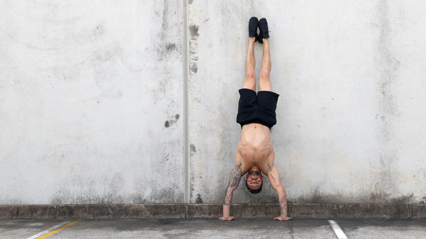 Centr trainer Luke Zocchi performs a handstand shirtless against a wall.