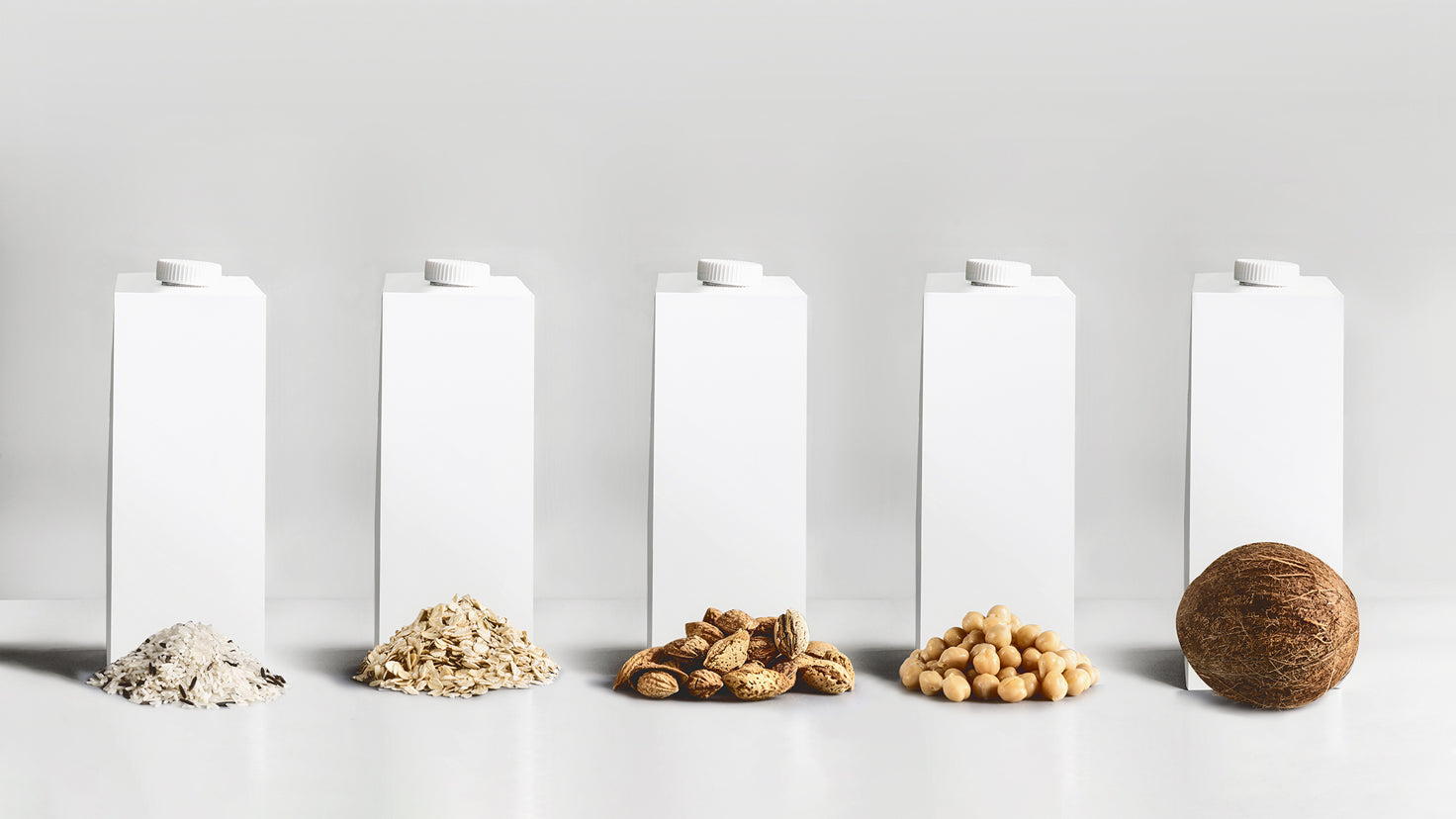 Cartons of plant-based milks with their ingredients laid in front of them.