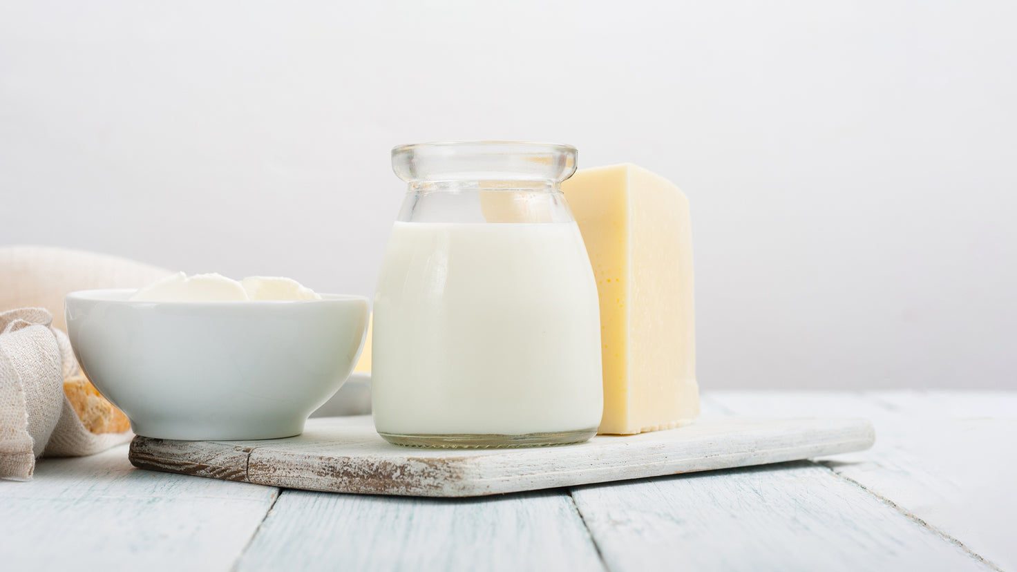 A glass of milk sits next to a block of cheese and a bowl of cream.