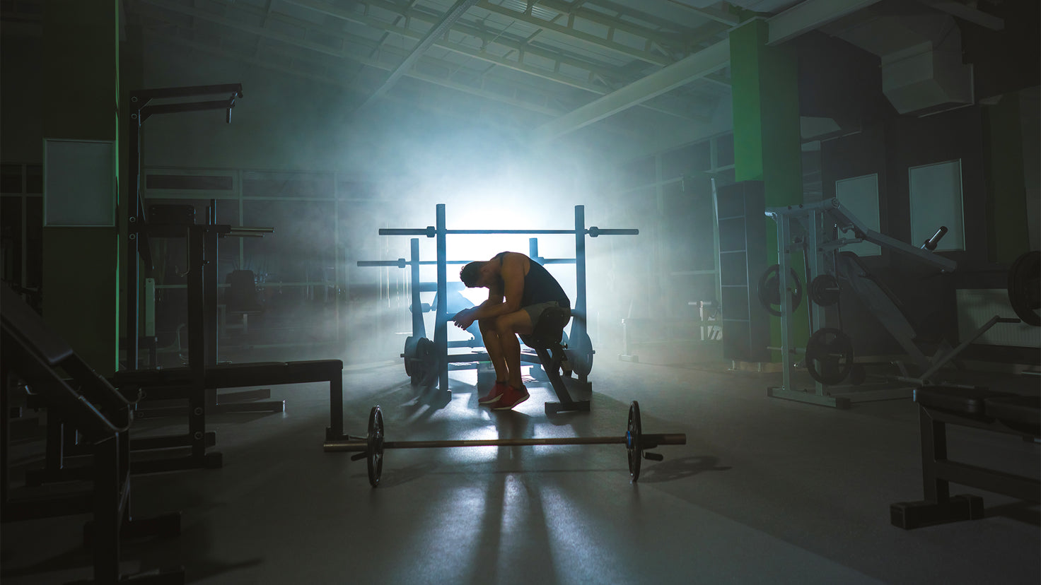 An exhausted man slumped over in an empty gym at dawn.