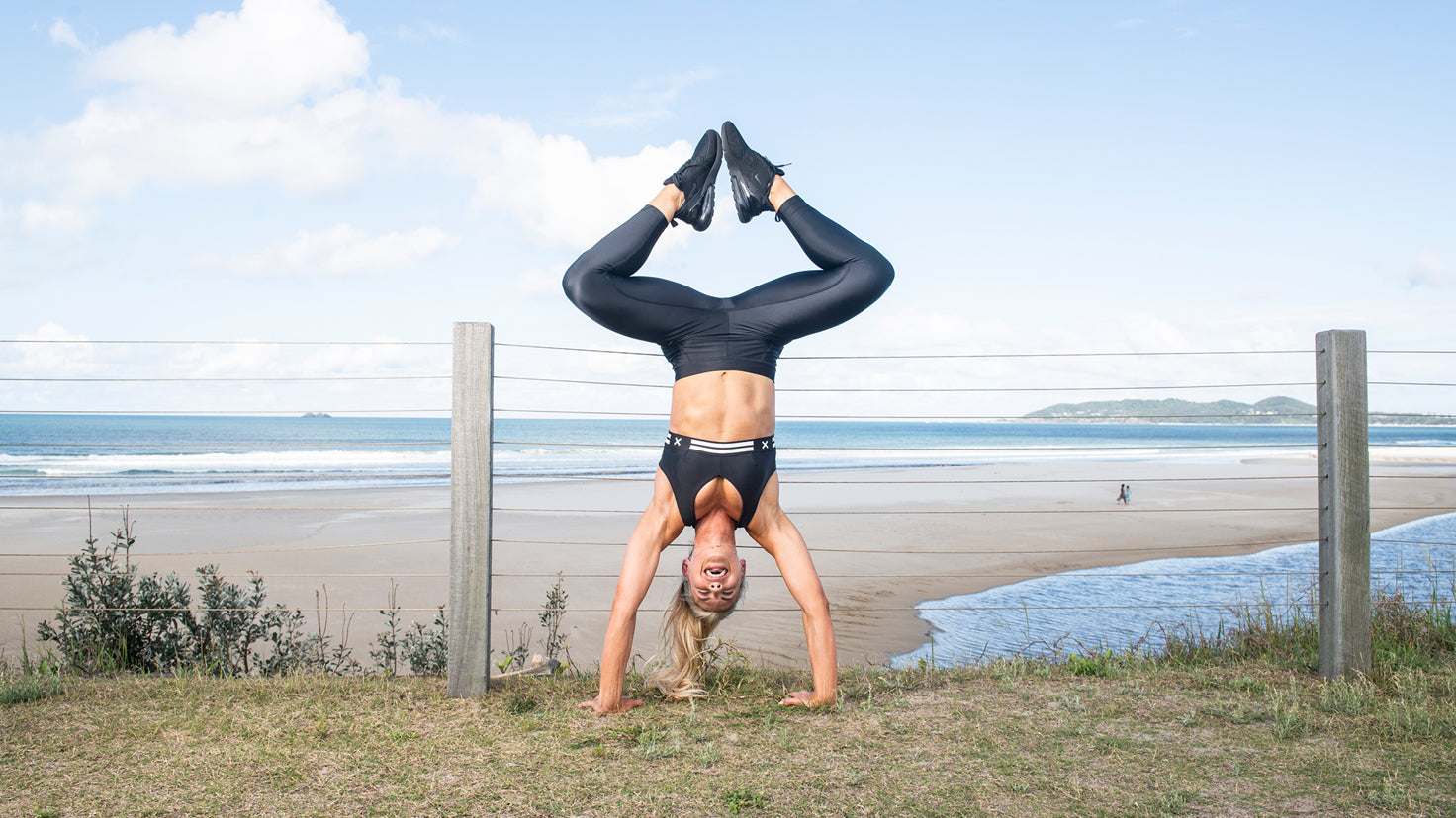 Tiffiny Hall does a handstand with bent legs on the beach.