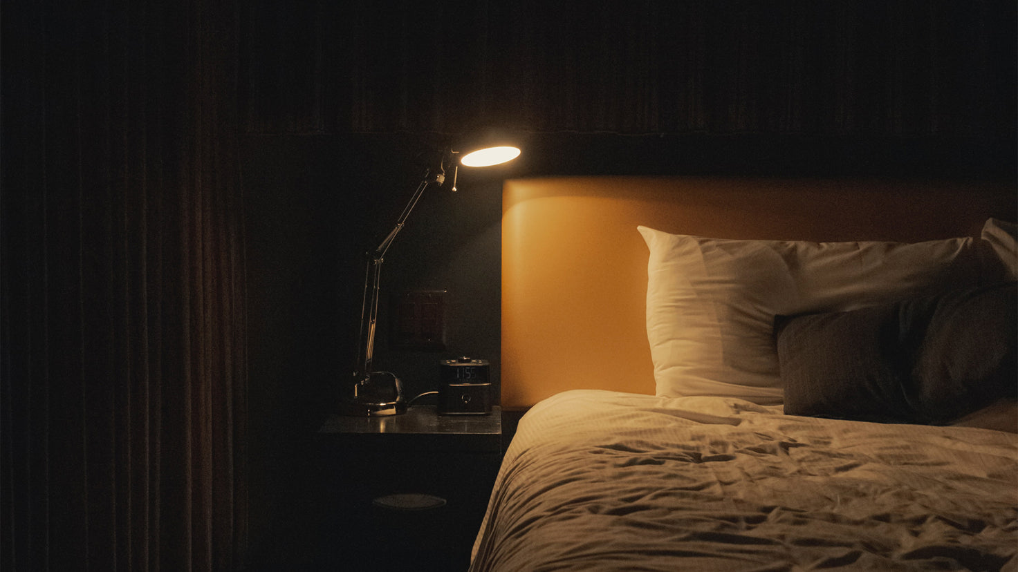A bedside lamp shines on an empty bed, abandoned due to insomnia.
