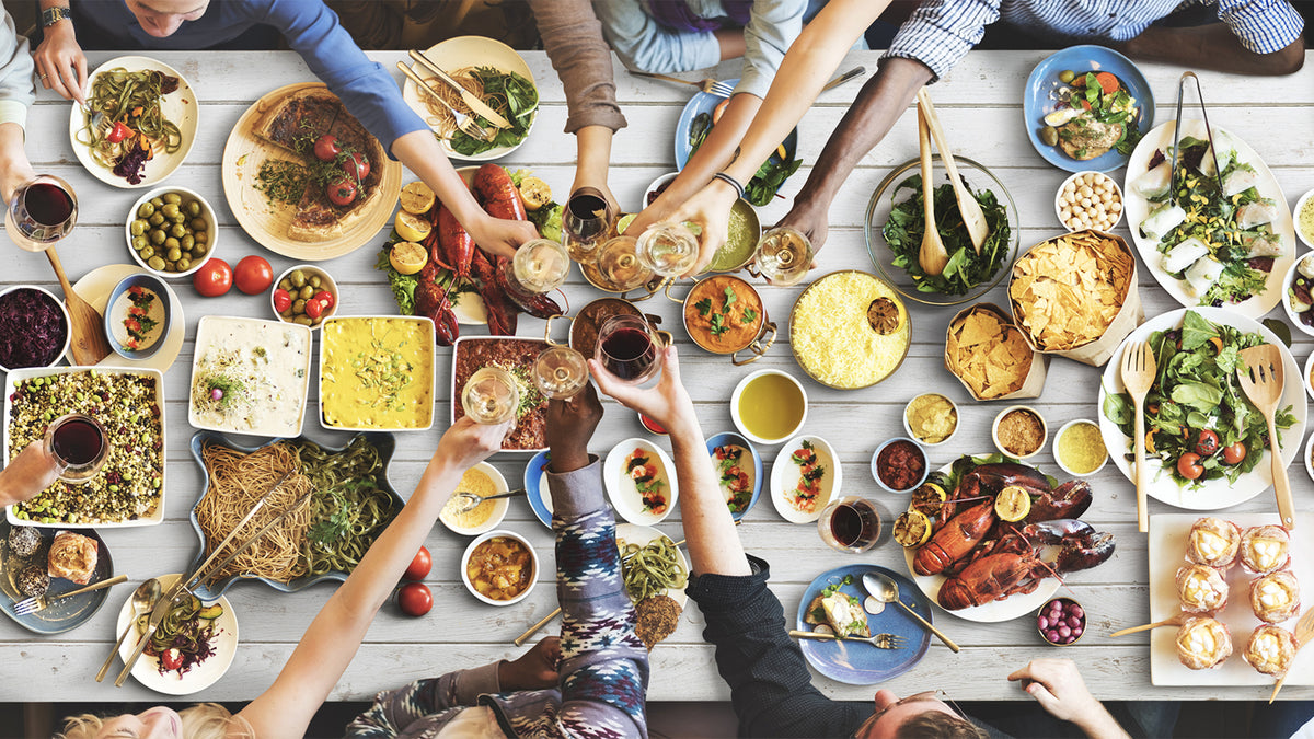 A group of friends clink wine glasses over a table filled with various food dishes.