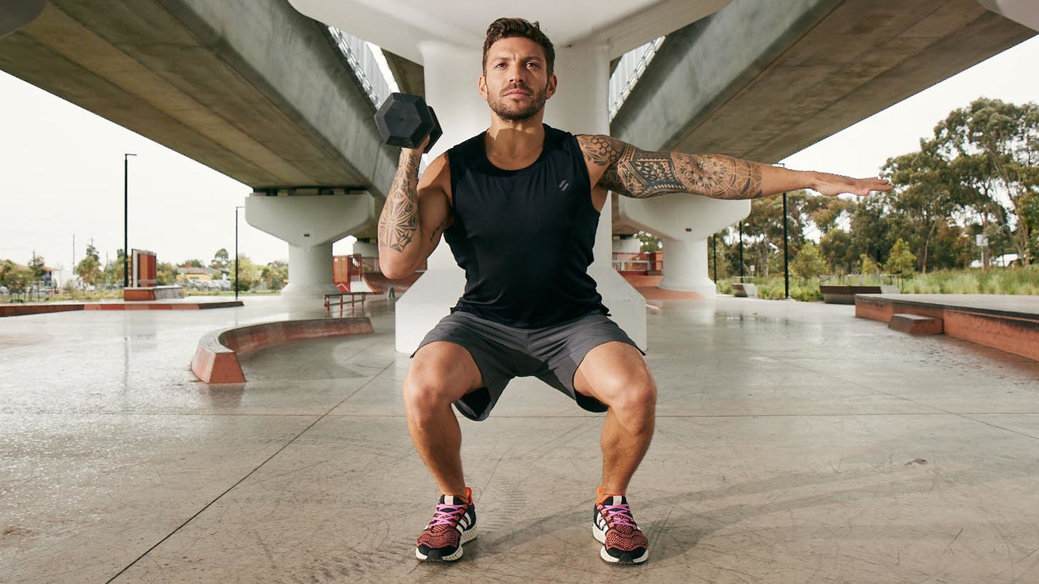 Centr trainer Luke Zocchi performs a squat while pressing a dumbbell with his right hand and his lef