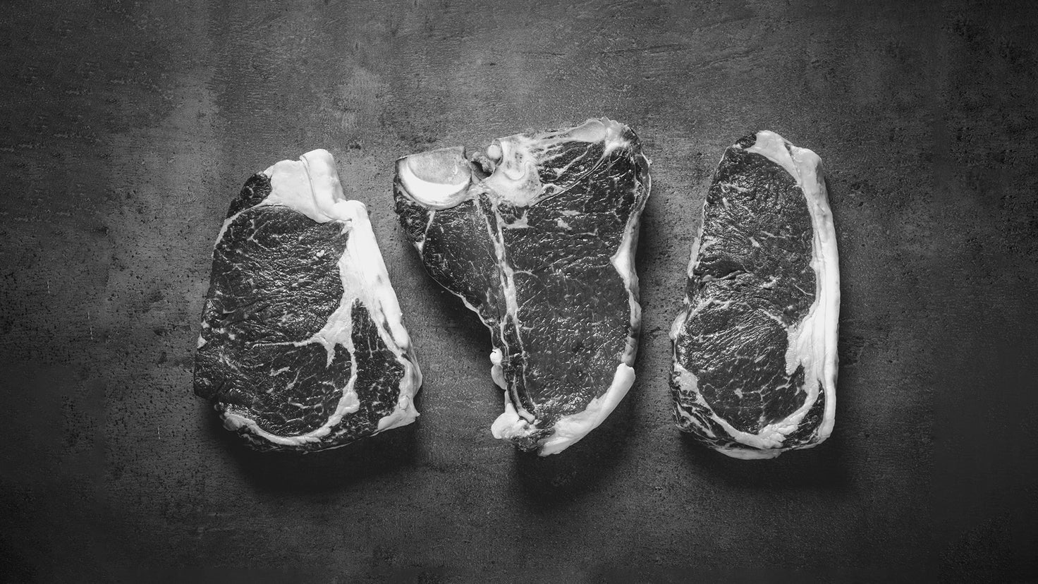 Black and white flat lay of three raw steaks.