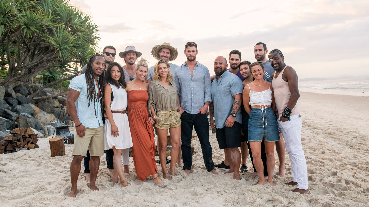 Chris Hemsworth stands with Centr's trainers and experts on a sandy beach.