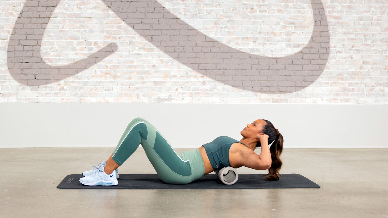 Centr trainer Maricris Lapaix performs an upper back stretch using a foam roller from the Centr Reco