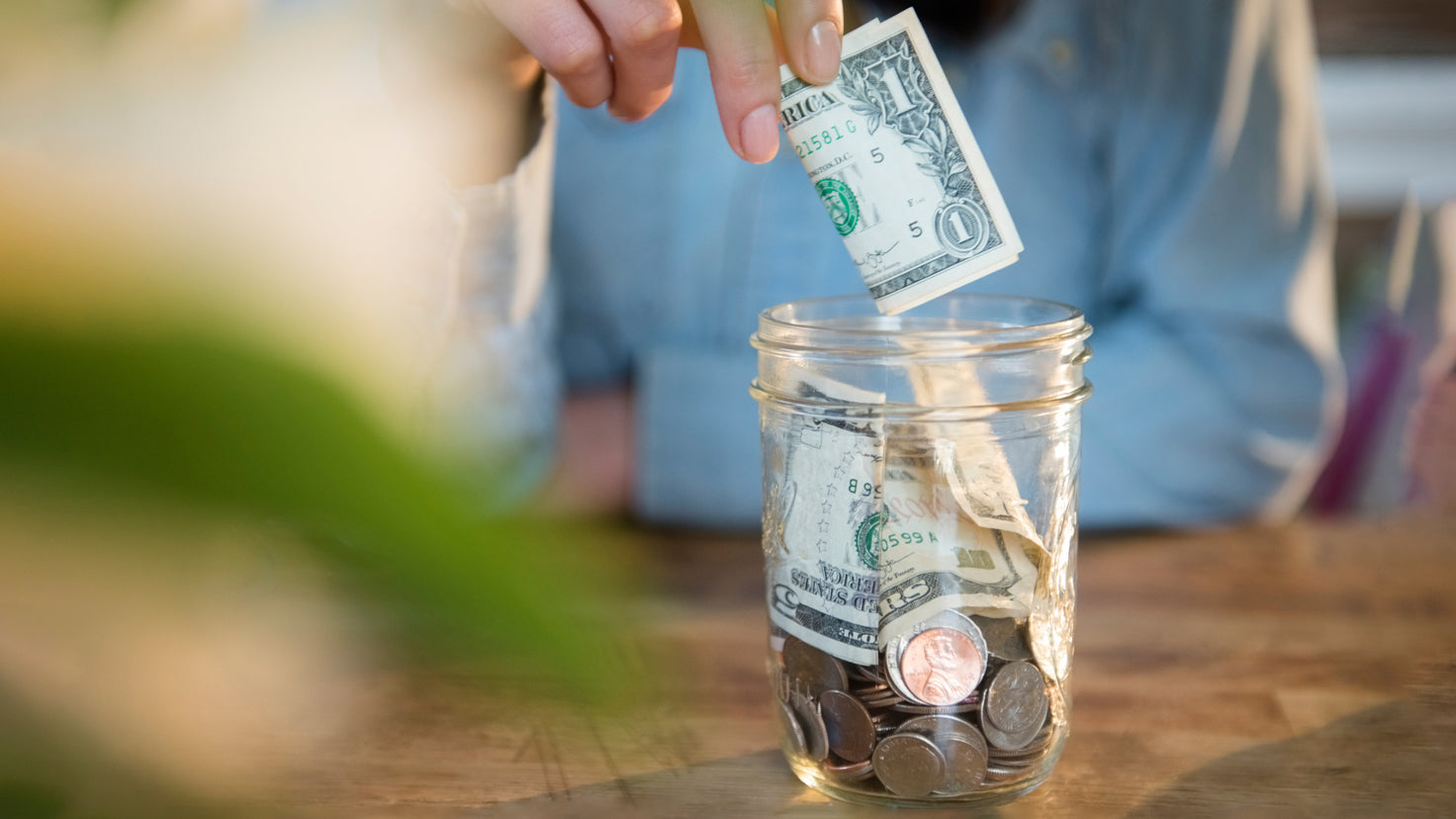 Someone places a US one-dollar bill into a glass jar.
