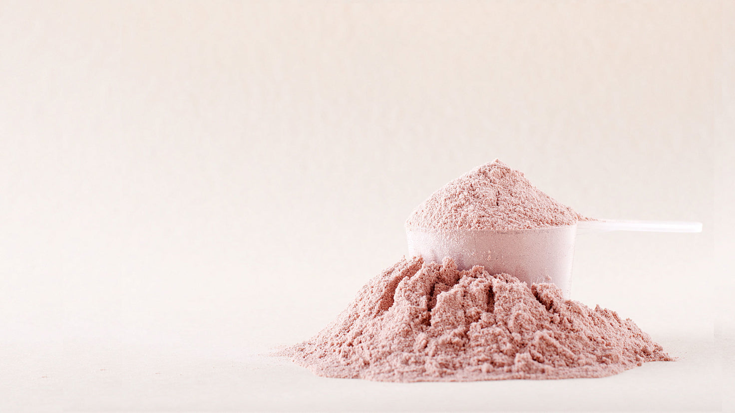 A large scoop of pink protein powder, next to a heaped pile of protein powder.