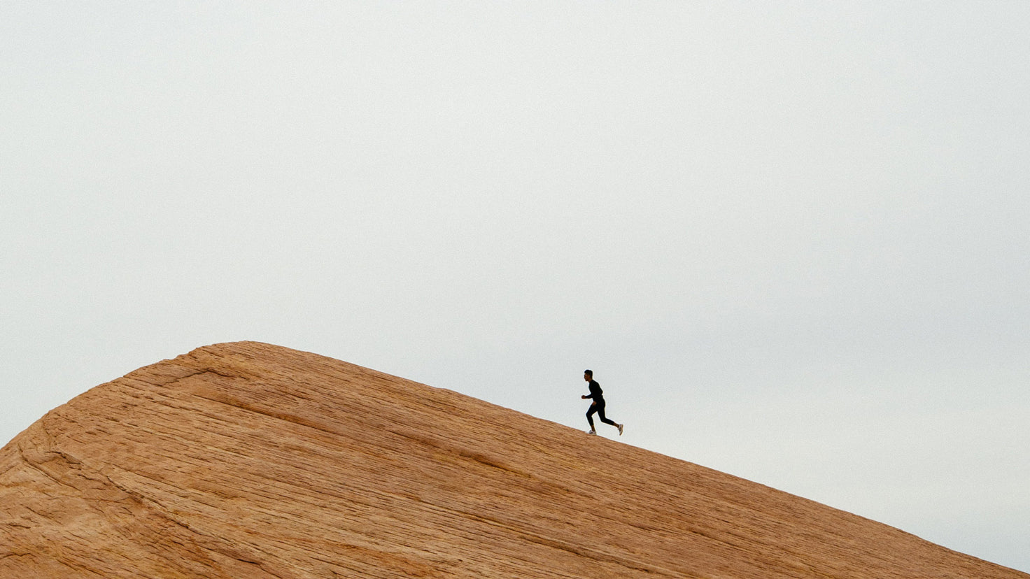 A wide shot of a man running up a large slanted rock face.