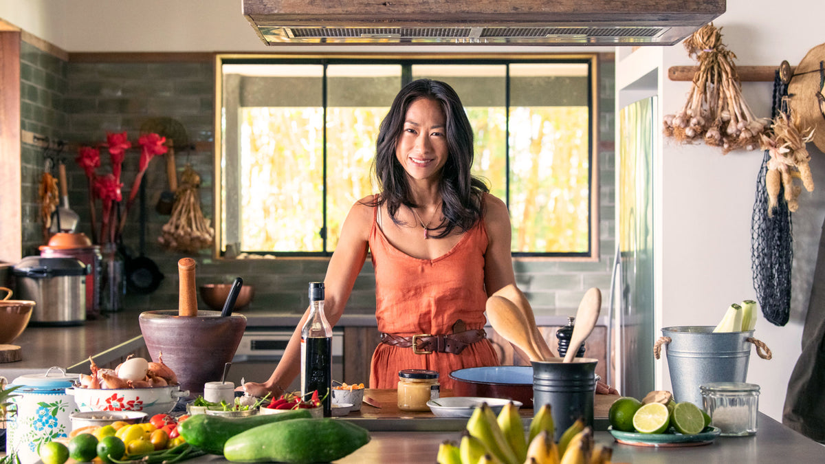 Palisa Anderson stands in a sunlit kitchen surrounded by produce.