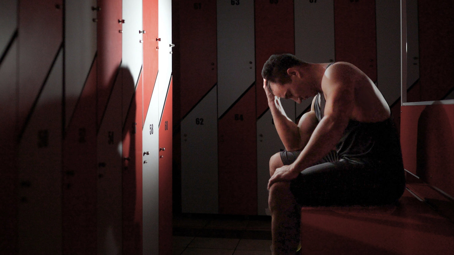 A man sits in a locker room with his head in his hands.