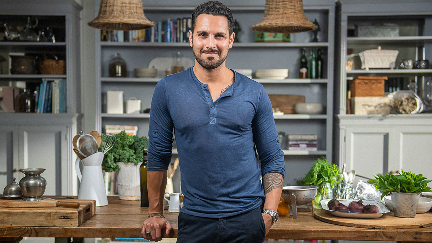 Sergio Perera leaning on a wooden kitchen bench, smiling.