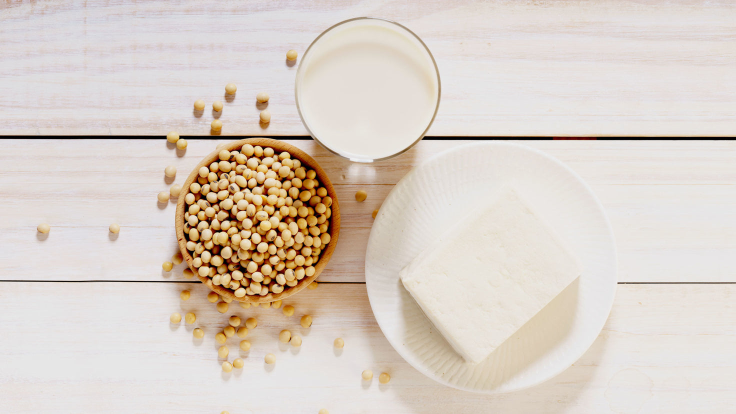 Soy beans, firm tofu and soy milk on a wooden surface.