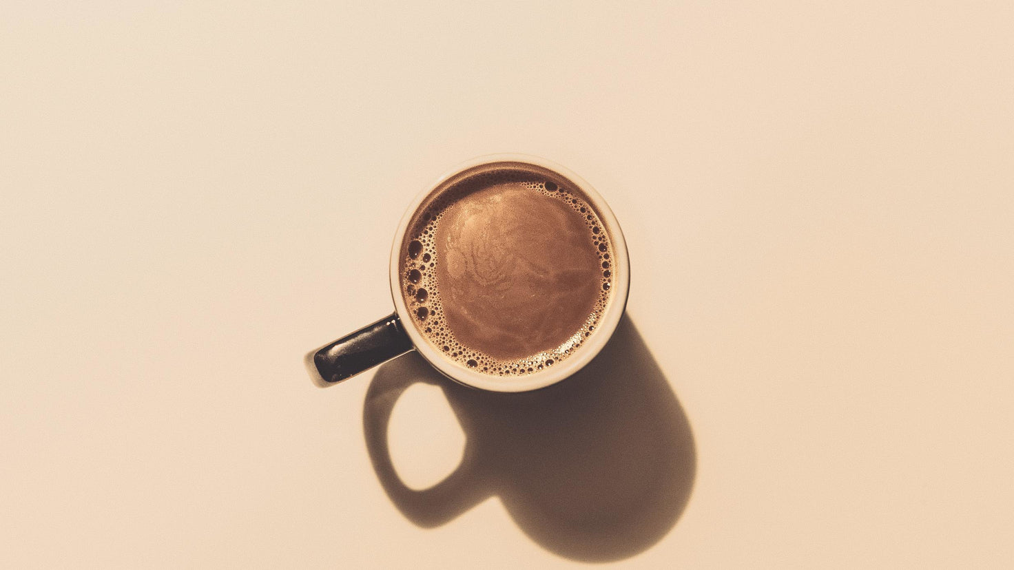 A fresh cup of coffee, seen from above against a cream-coloured background.
